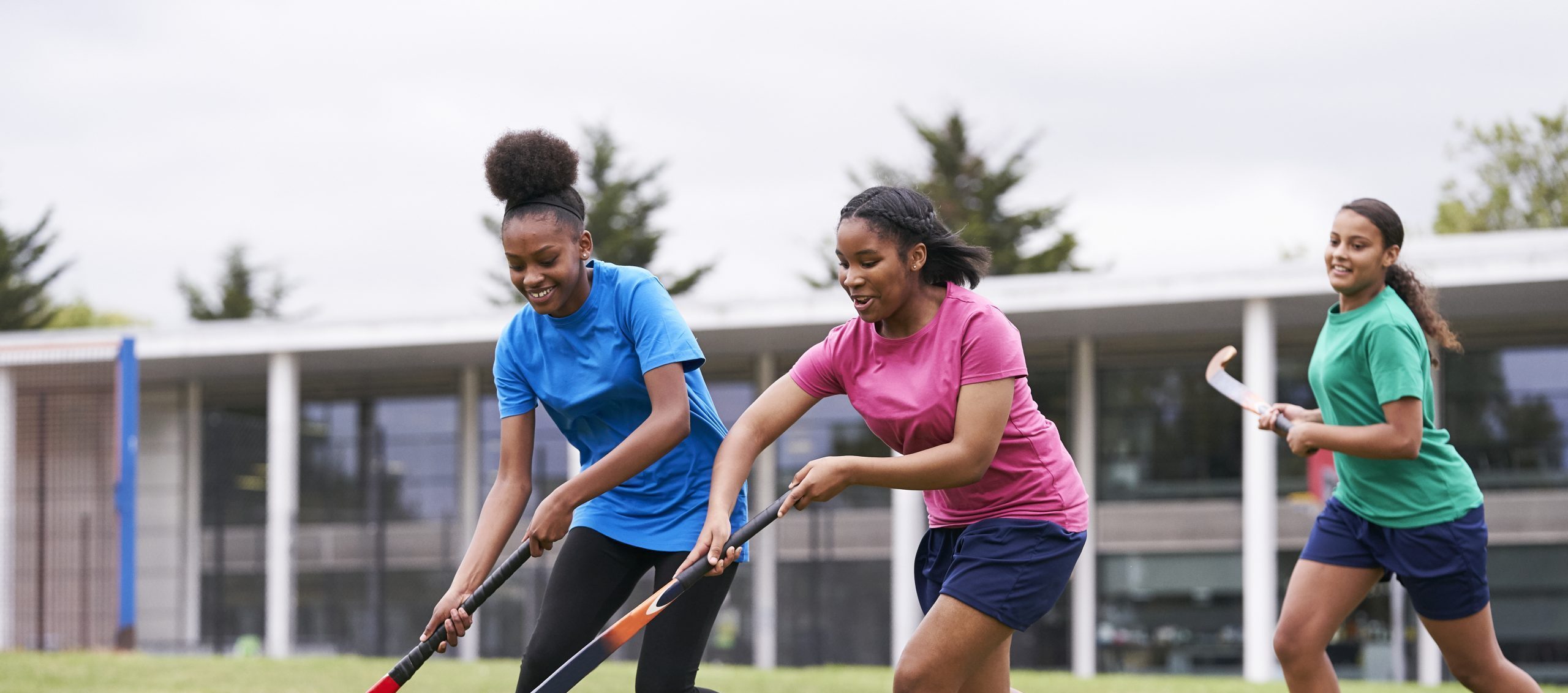 Two black teenage school girls playing hockey on grass