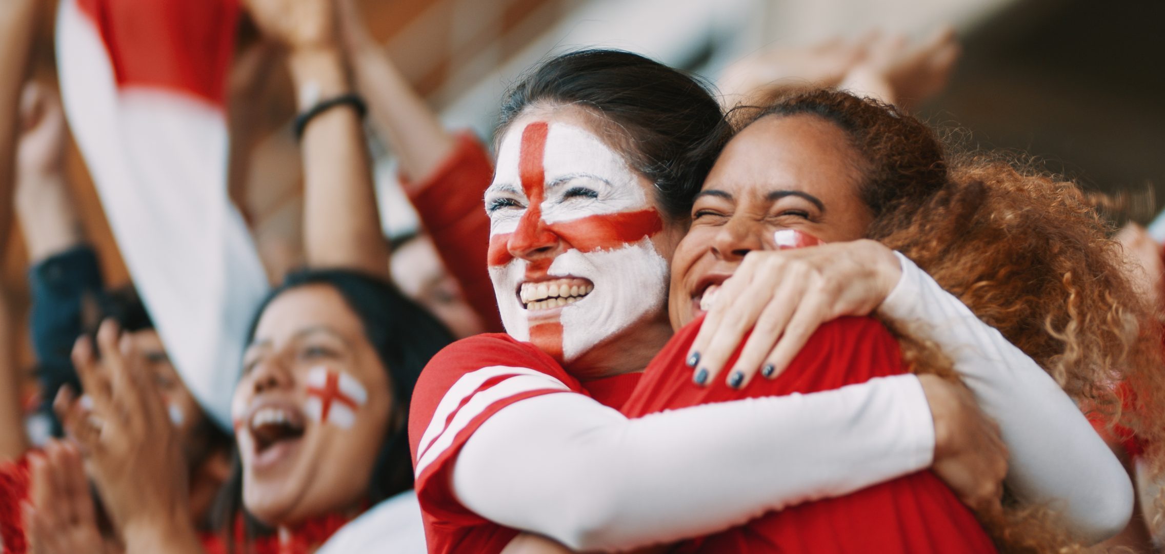 Two female football fans celebrating a goal. One has the England flag painted on her face