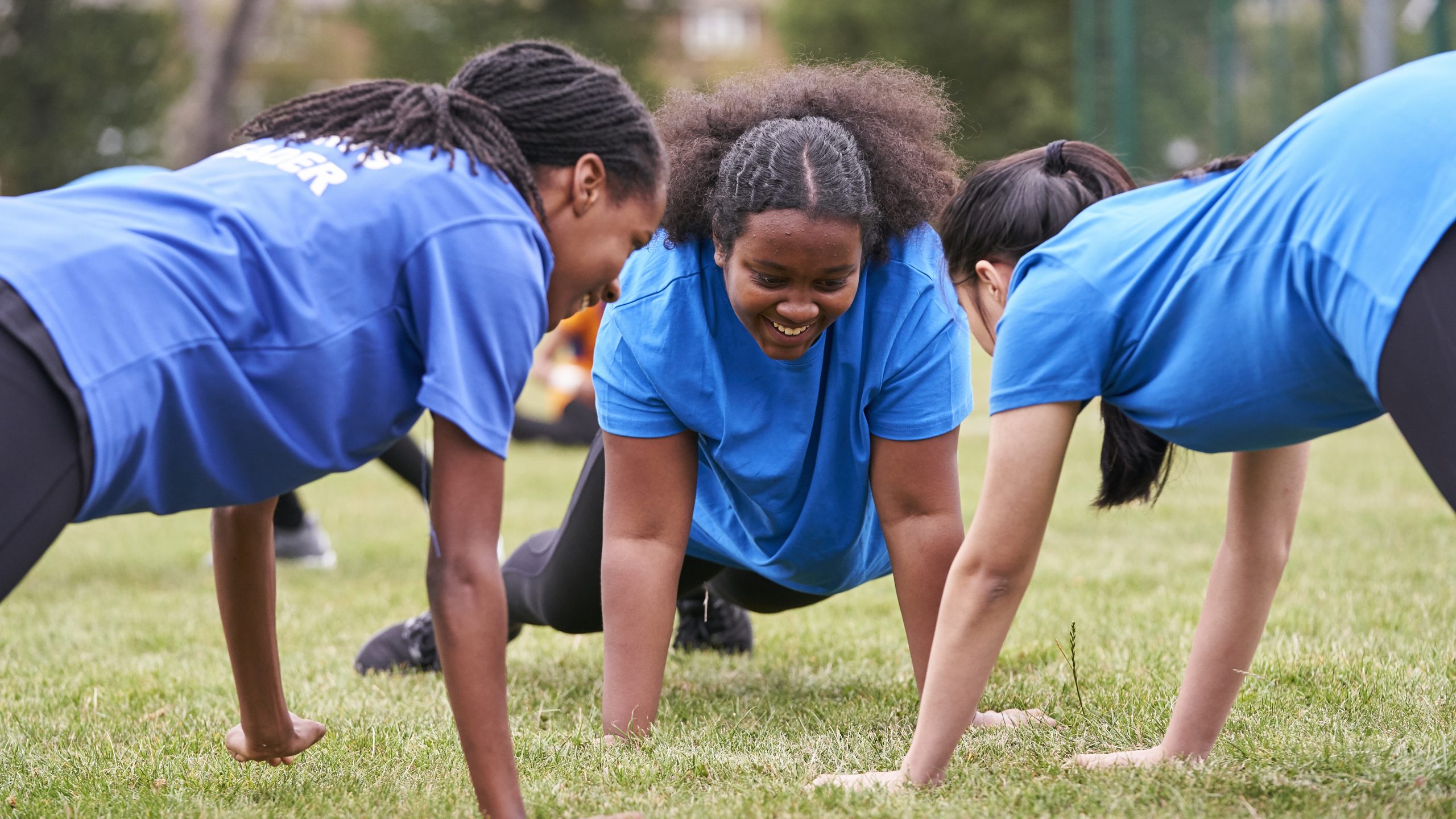 Three black teenagers planking on grass