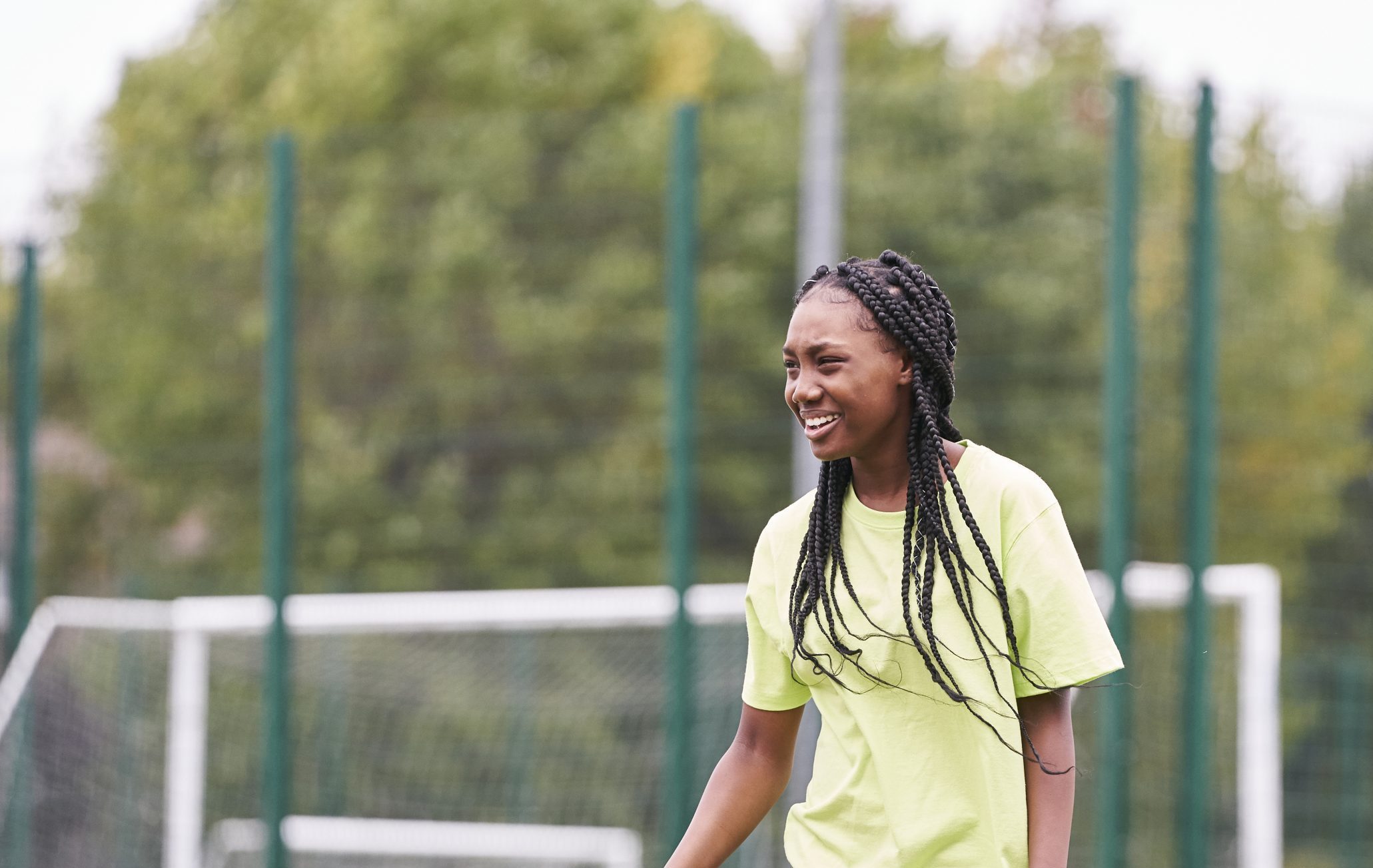 A young black teenager with braided hair laughing while playing football